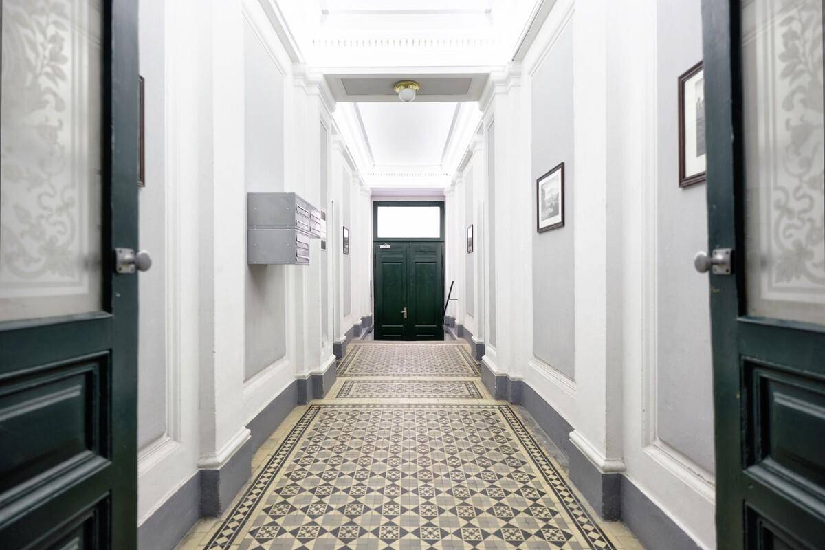 Langer Flur mit gemustertem Fliesenboden, hohen Decken und eleganten Türen in einem Altbau.