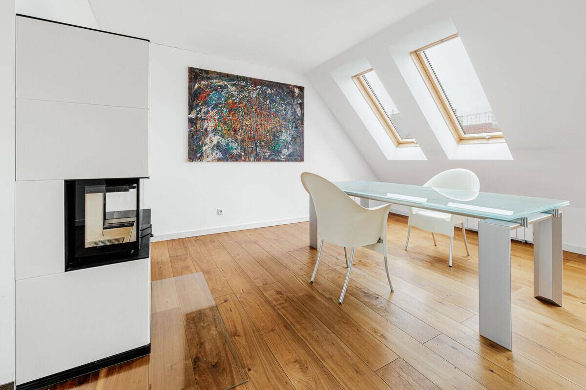 Detailansicht des Essbereichs mit elegantem Glastisch, Kamin und viel Tageslicht durch die Dachfenster.