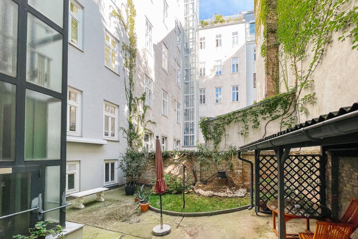 Gepflegter Innenhofgarten mit Sitzbereich und moderner Glasfassade des Gebäudes.