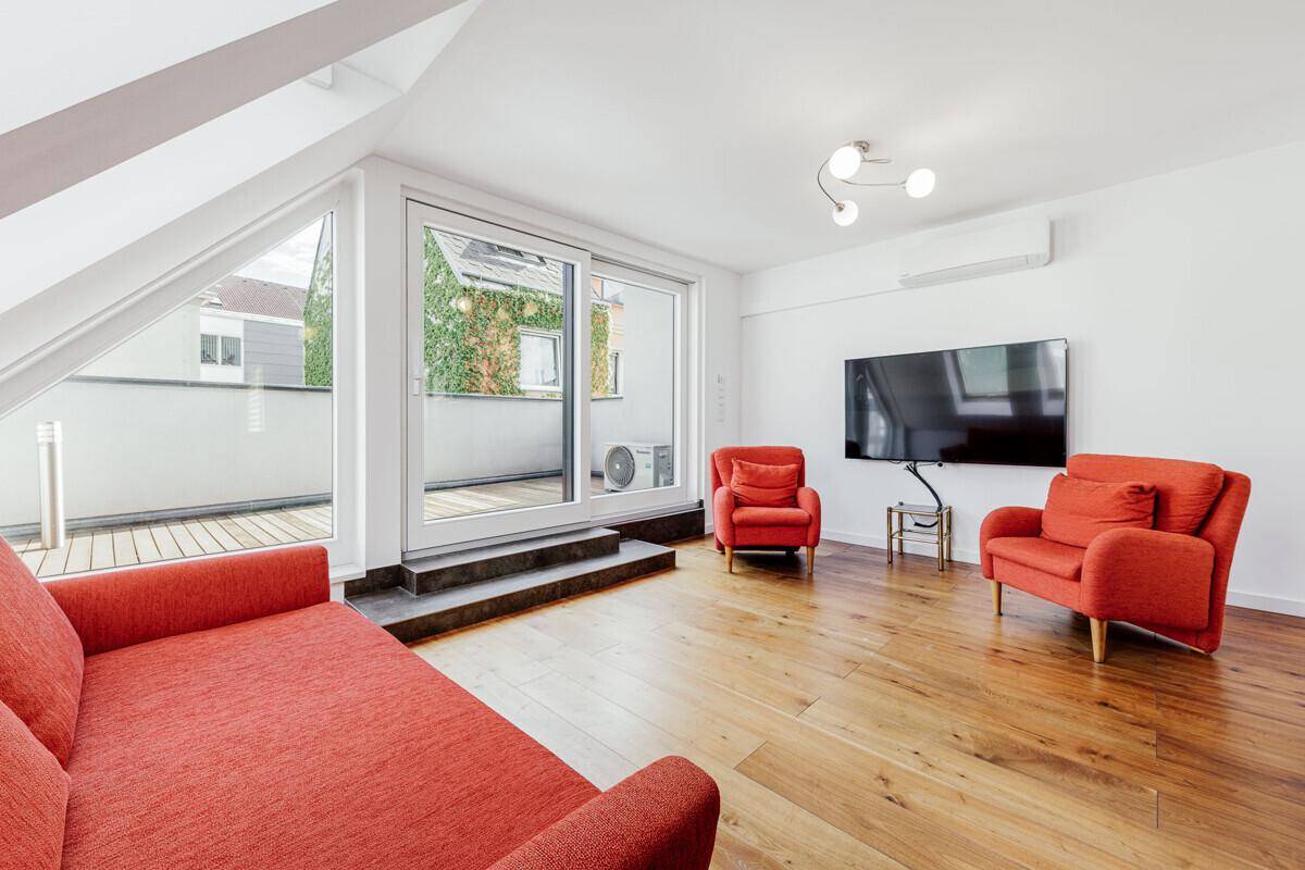 Helles Wohnzimmer mit roten Sofas, Wandfernseher, Klimaanlage und direktem Balkonzugang.