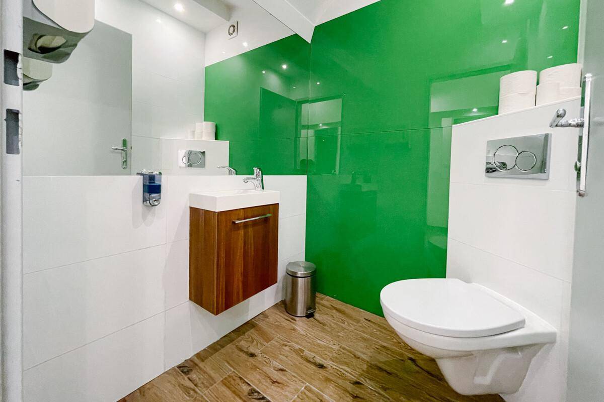 Modernes Gäste-WC mit grüner Akzentwand, Holzwaschtisch und wandhängendem WC.