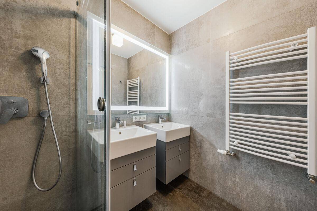 Modernes Badezimmer mit Doppelwaschbecken, begehbarer Dusche und beheiztem Handtuchhalter.