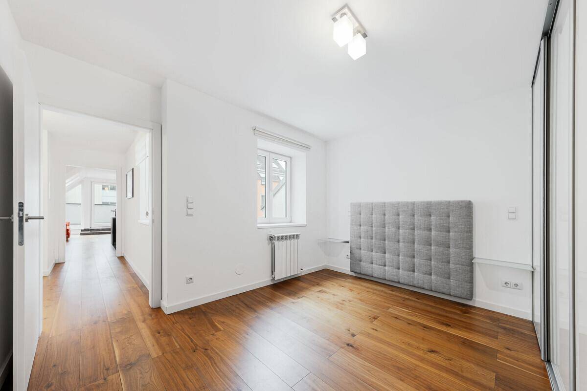 Helles Schlafzimmer mit Holzboden, Fenster und einem modernen, gepolsterten Kopfteil an der Wand.