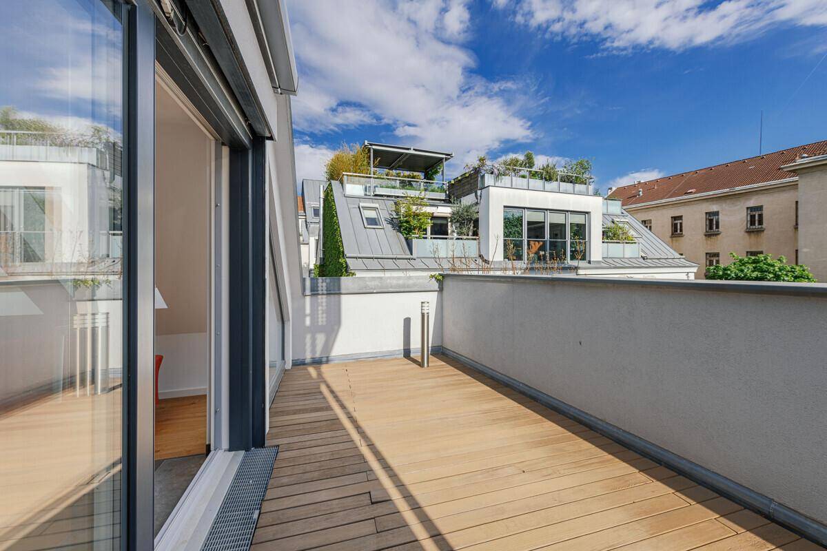Balkon mit Holzbelag und weitem Blick über die Dächer der umliegenden Gebäude.