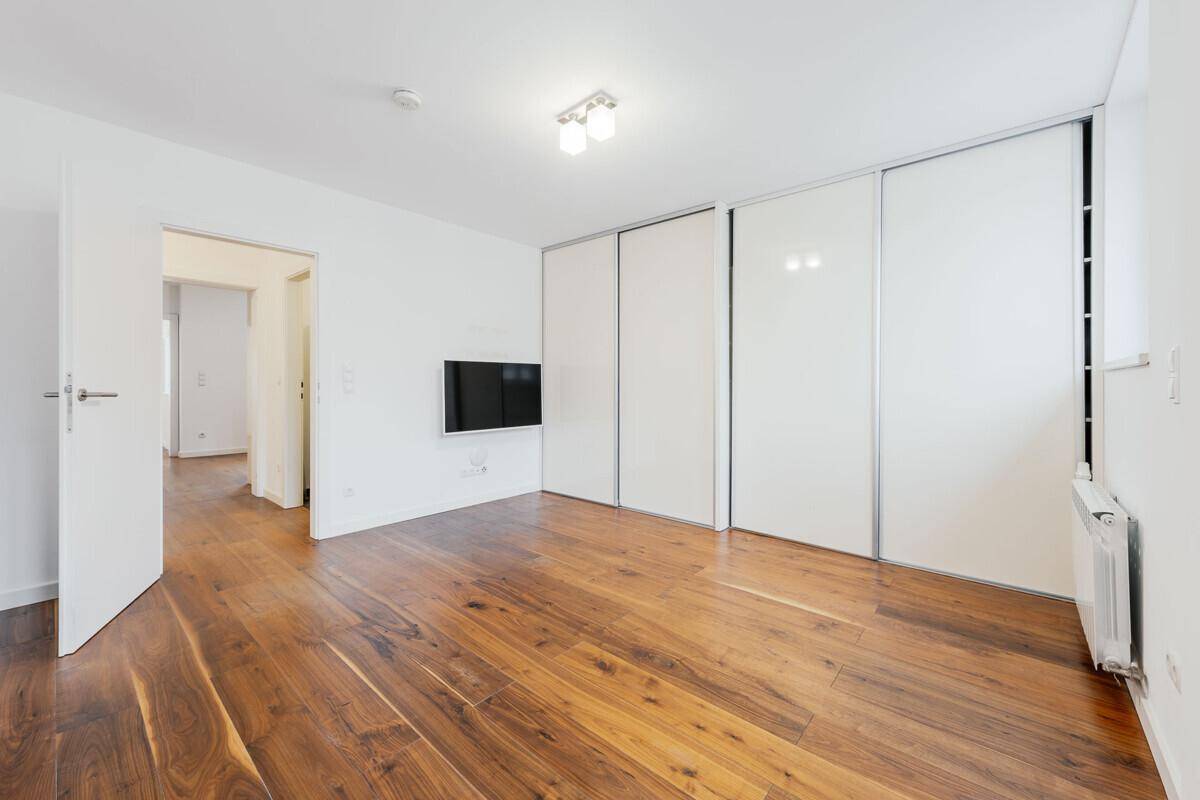 Schlafzimmer mit Holzboden, großen weißen Schiebetürenschränken und einem Wandfernseher.