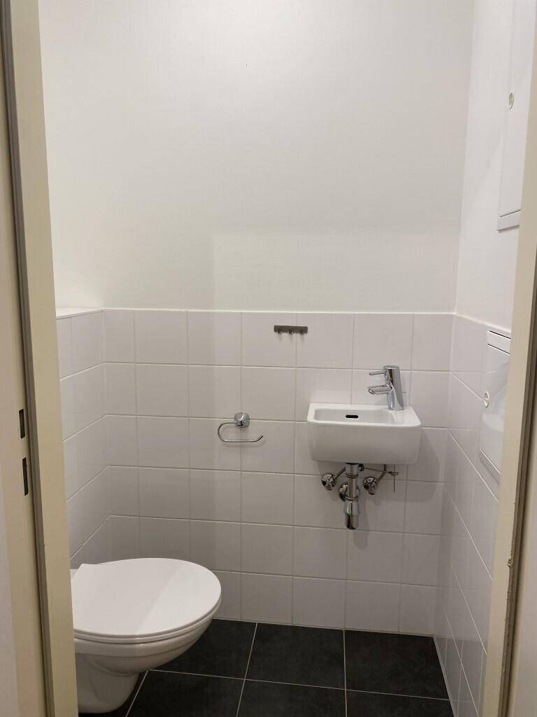 Kleines Gäste-WC mit weißen Fliesen, dunklem Boden, Toilette und einem kompakten Waschbecken.