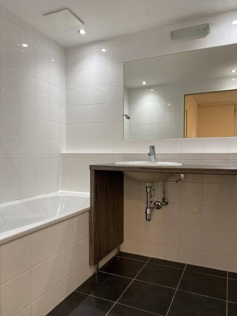Modernes Badezimmer mit weißen Fliesen, dunklem Boden und einer Badewanne mit integriertem Waschtisch.