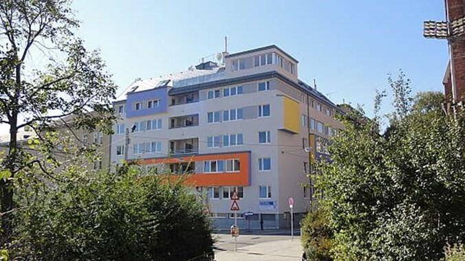 Modernes Mehrfamilienhaus mit farbigen Akzenten und großen Fenstern, umgeben von Bäumen.