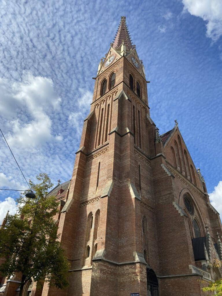 Beeindruckende historische Backsteinkirche mit hohem Turm unter einem bewölkten blauen Himmel.