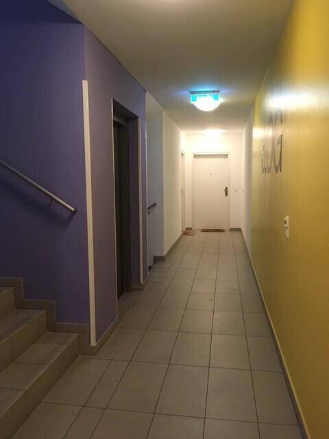 Heller Flur mit Fliesenboden, farbigen Wänden und Zugang zu einem Aufzug und Treppenhaus.