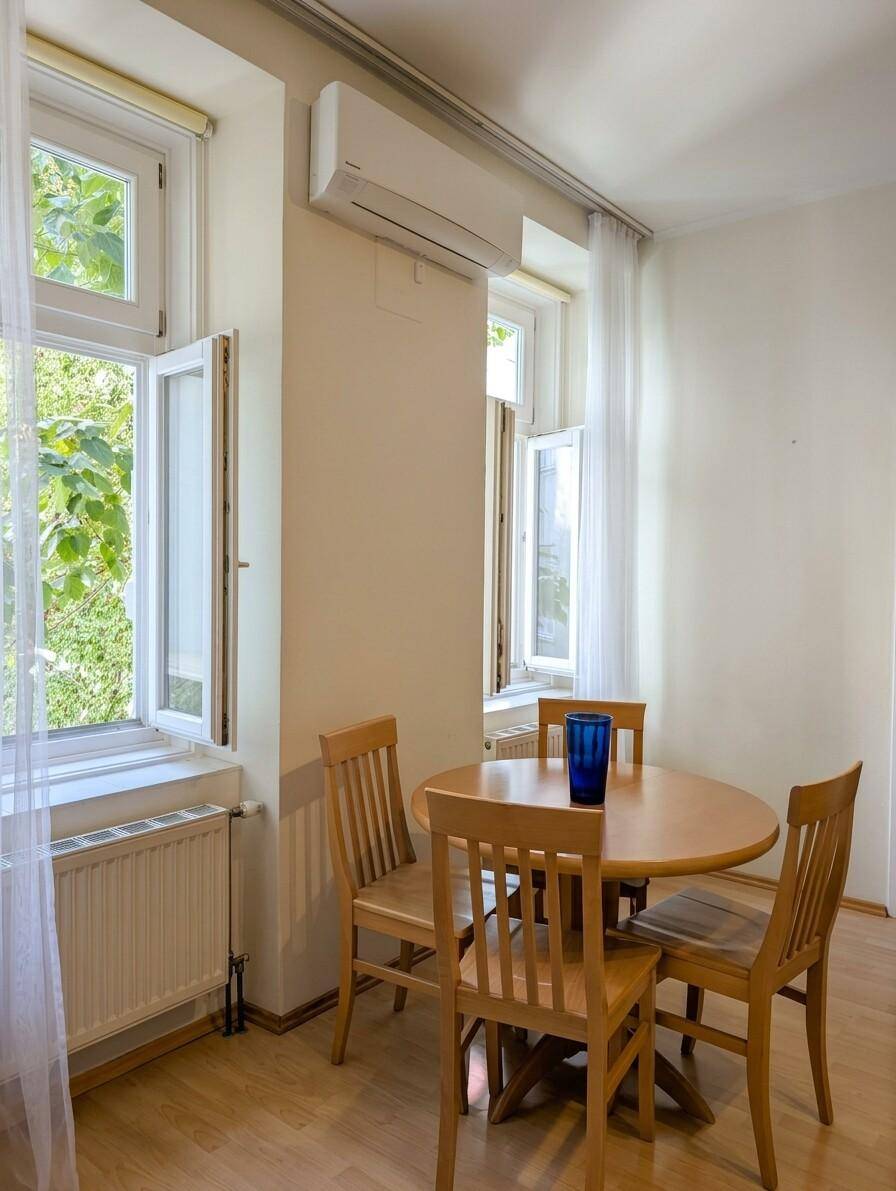 Heller Essbereich mit Holztisch und Stühlen, Klimaanlage und Blick ins Grüne.
