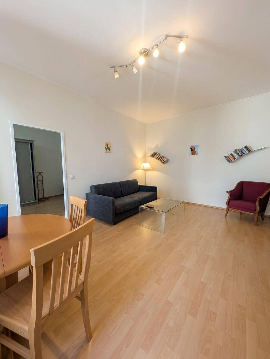 Geräumiger Wohn-Essbereich mit Holzboden, Sofa, Glastisch und einem roten Sessel.