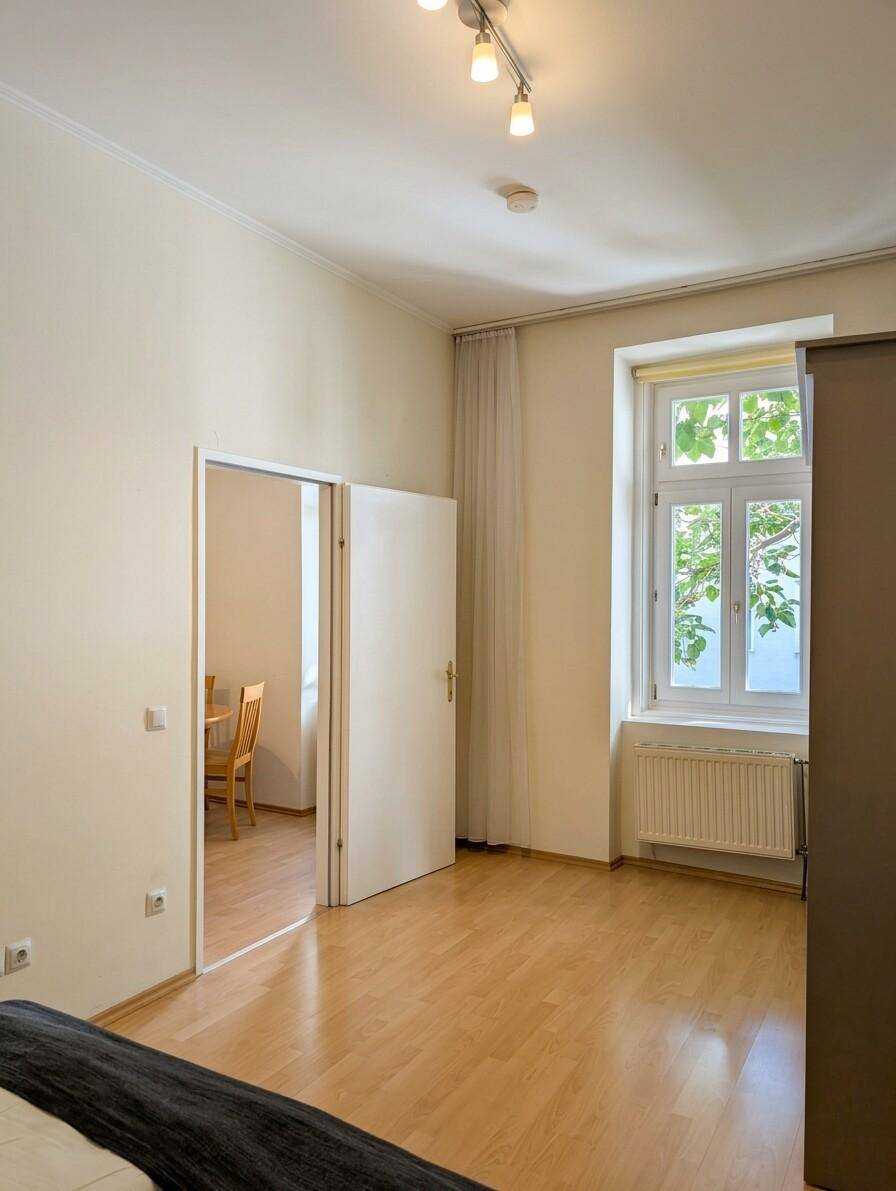 Schlafzimmer mit Laminatboden und Blick durch die offene Tür in den Essbereich.
