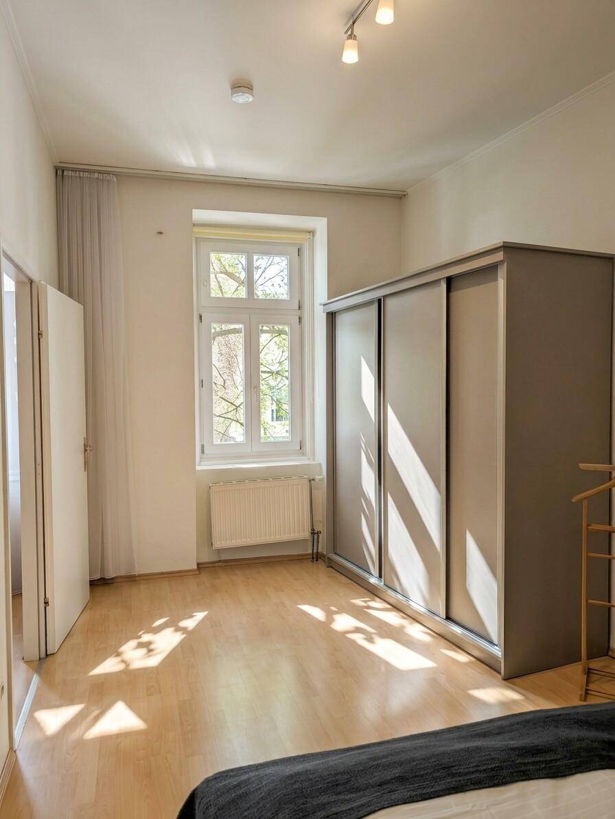 Schlafzimmer mit großem Schiebetürenschrank, hellem Fenster und Laminatboden.