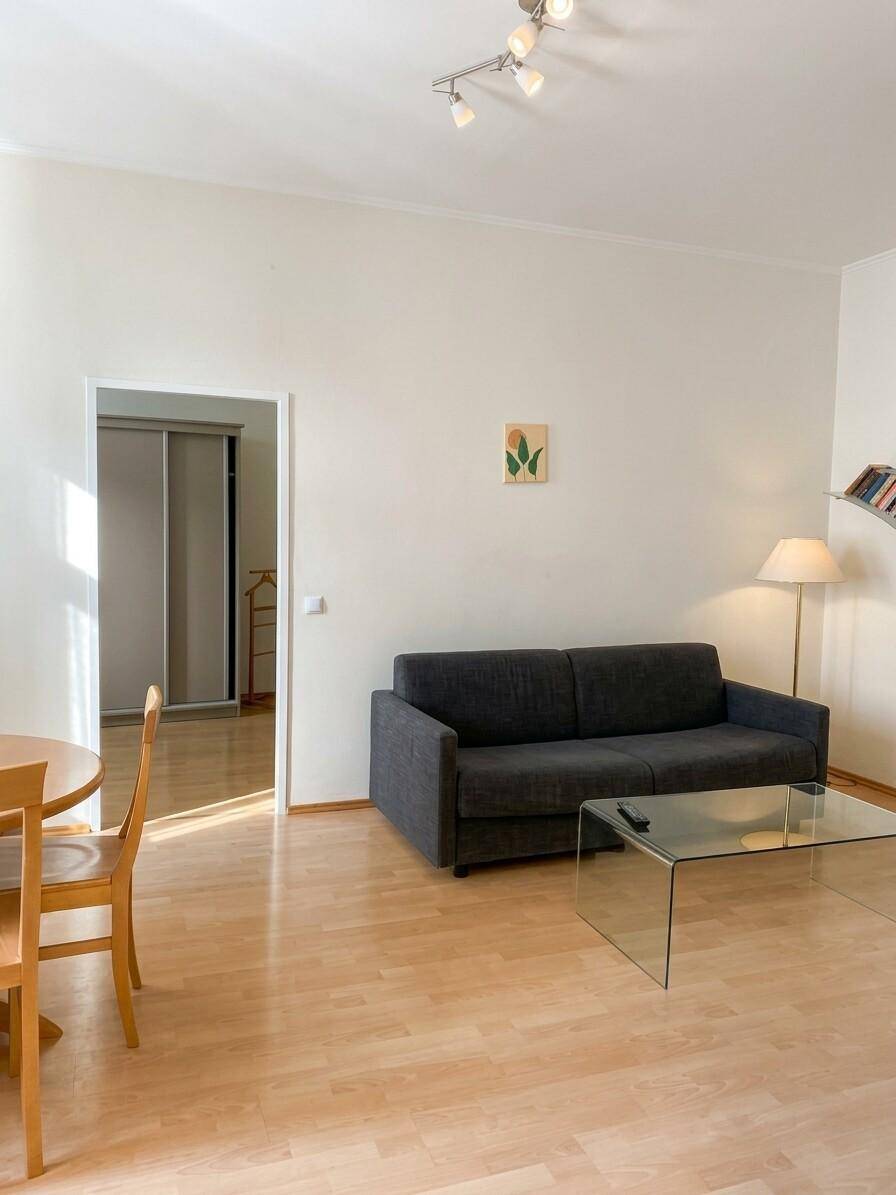 Heller Wohnbereich mit dunklem Sofa, Glastisch und Holzboden.