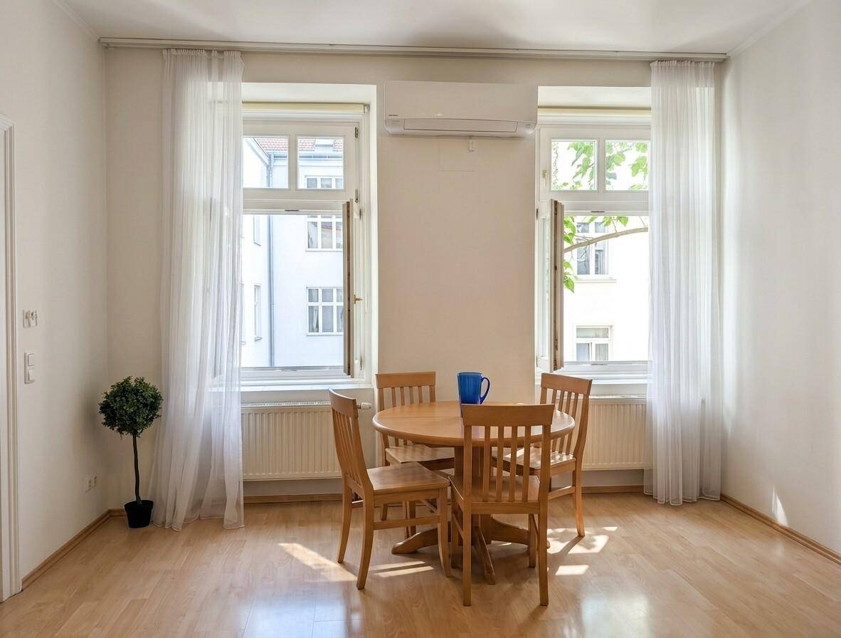 Essbereich mit Holztisch und Stühlen, umgeben von hellen Fenstern und Vorhängen.