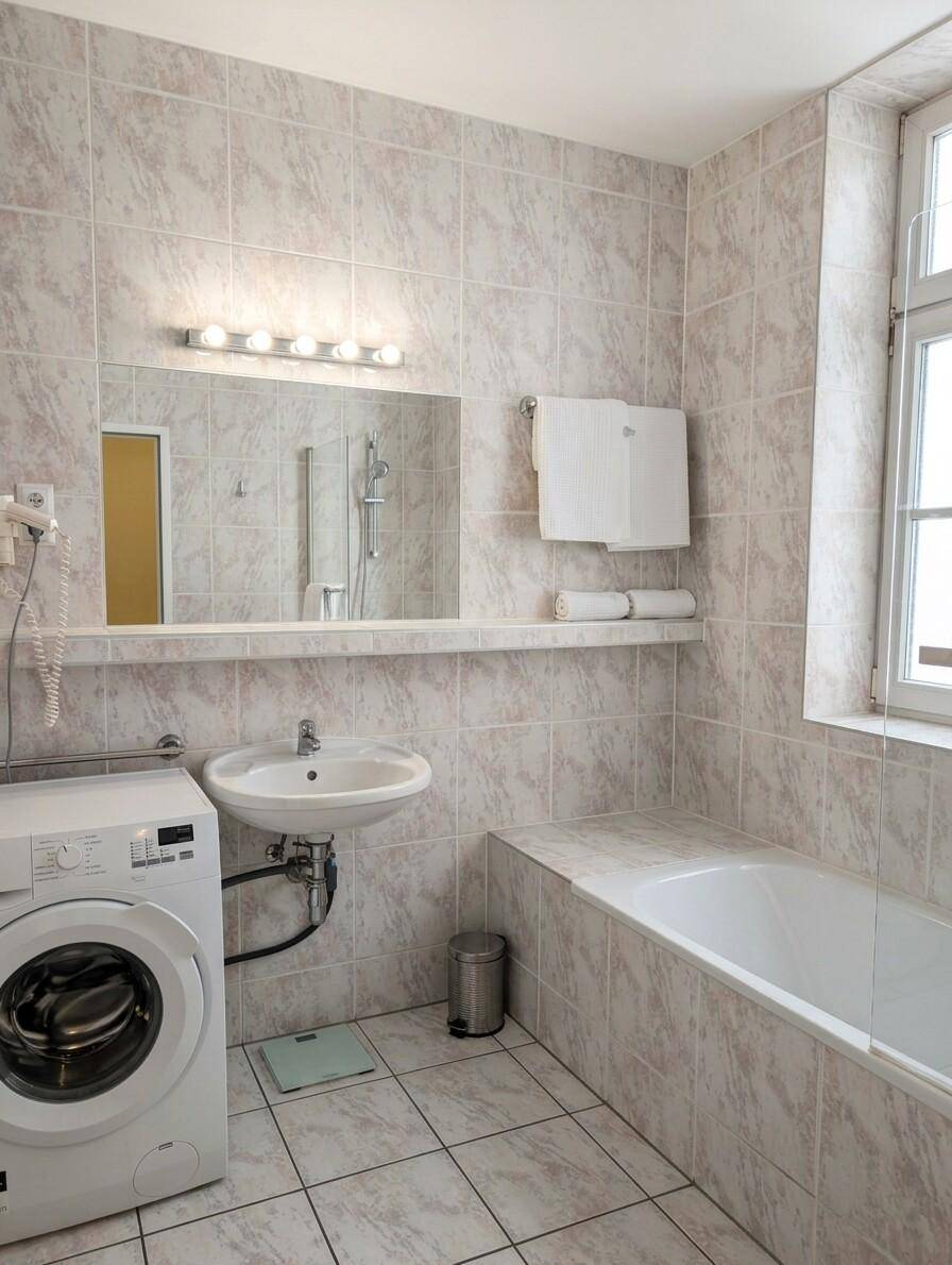 Gefliestes Badezimmer mit Badewanne, Waschbecken, Spiegel und Waschmaschine.