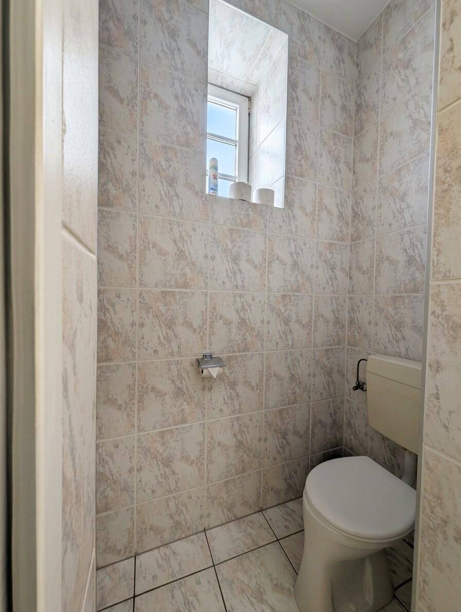 Kleines WC mit Toilette, Fenster und vollständig gefliesten Wänden und Boden.