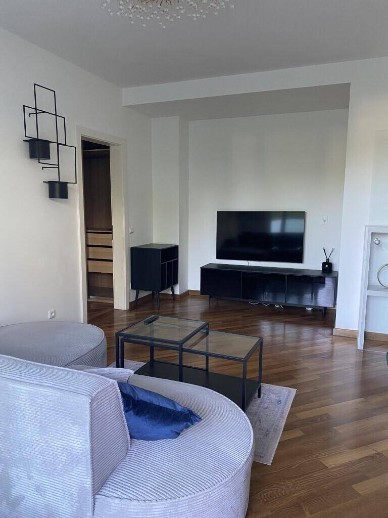 Wohnzimmer mit Fernseher, Holzboden und Blick in einen begehbaren Schrankbereich.