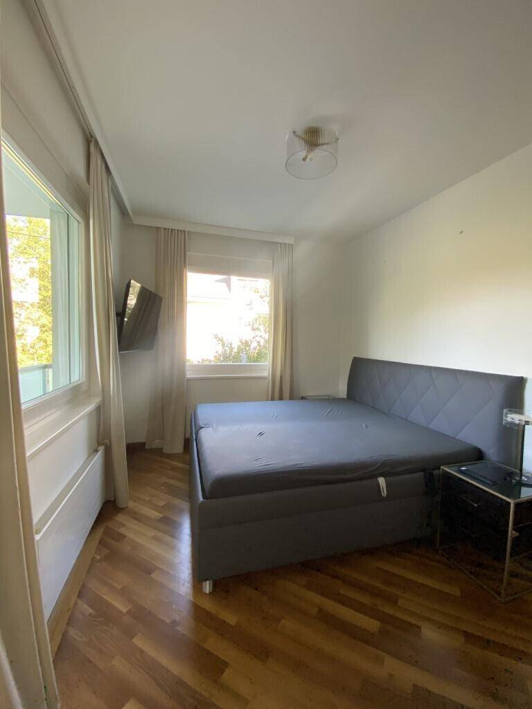 Helles Schlafzimmer mit Holzboden, großem Bett und viel Tageslicht durch die Fenster.