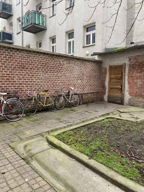 Hinterhofbereich mit Ziegelmauer, Holztür und gepflastertem Boden, mehrere Fahrräder abgestellt.