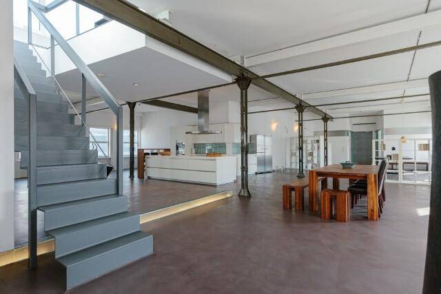 Weitläufiger Loft-Wohnraum mit offener Küche, Essbereich und moderner Treppe, geprägt von industriellem Charme.