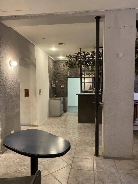 Innenansicht eines Sitzbereichs, der zu einer kleinen Küchenzeile oder Bar im Hintergrund führt, renovierungsbedürftig.