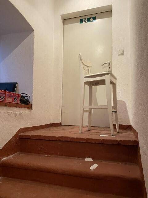 Treppenabsatz mit einer einfachen Tür und einem Hocker, der auf den nächsten Bereich des Gebäudes führt.