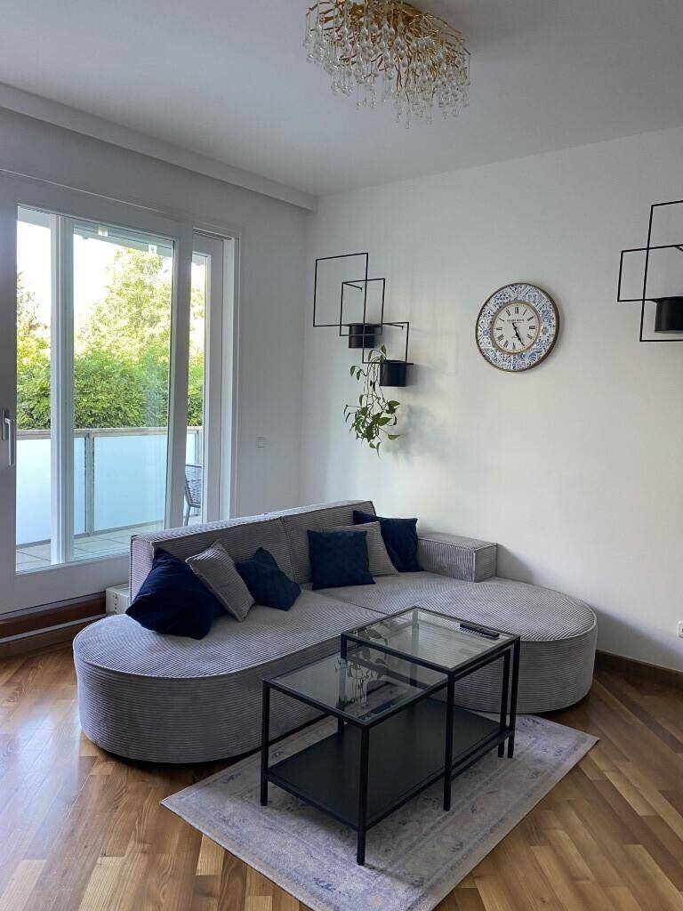 Gemütliches Wohnzimmer mit geschwungenem Sofa, Holzboden und großen Fenstern zum Balkon.