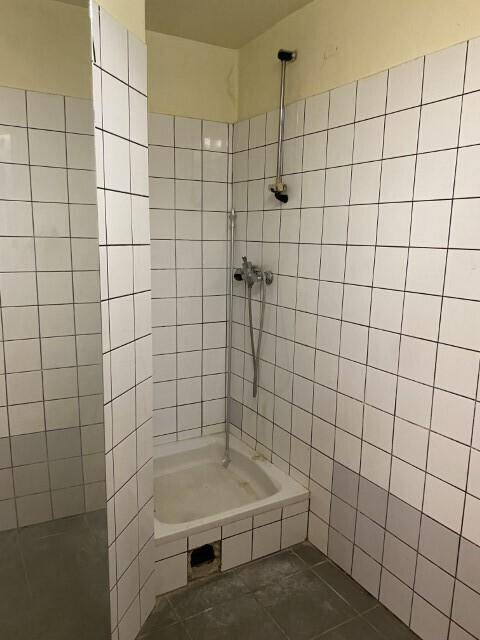 Einfacher Duschbereich mit weißen Wandfliesen und einer Duschwanne, der eine Renovierung benötigt.