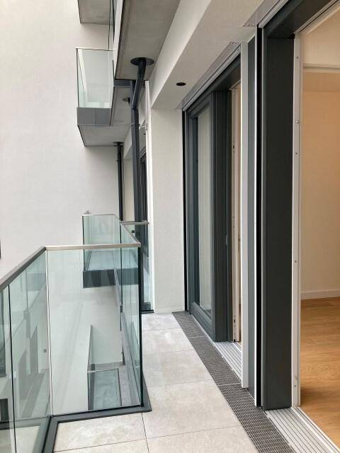 Moderner Balkon mit Glasgeländer und Fliesenboden, bietet einen Blick auf die umliegenden Gebäude.