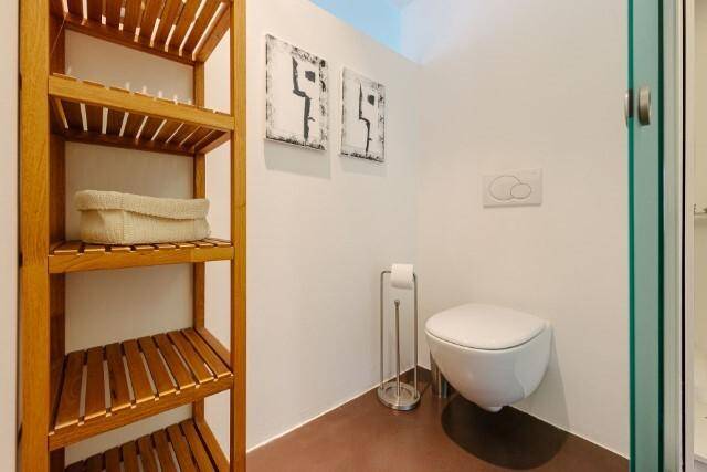 Modernes WC mit wandhängender Toilette und Holzregal in einem minimalistischen Design.