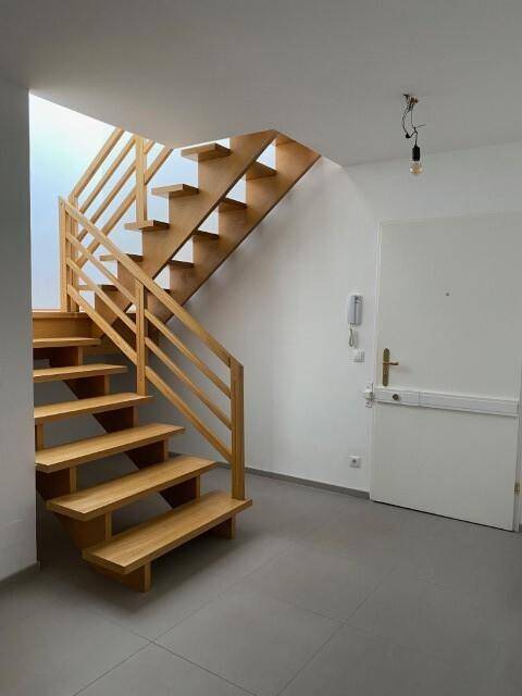 Heller Eingangsbereich mit moderner Holztreppe und Eingangstür, auf Fliesenboden.