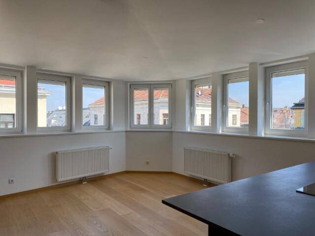 Heller, leerer Raum mit vielen Fenstern, Holzfußboden und Heizkörpern, ideal als Wohnbereich.