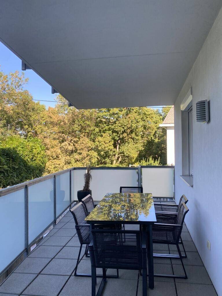 Heller Balkon mit Terrassenmöbeln, Fliesenboden und Blick ins Grüne.