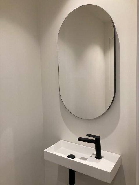 Kleines Gäste-WC mit modernem Waschbecken und ovalem Spiegel, stilvoll und platzsparend.