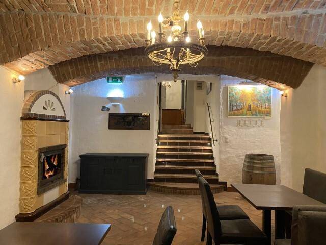 Gemütlicher Restaurantbereich mit einem Kamin, einer Holztreppe und traditioneller Einrichtung unter einer Gewölbedecke.