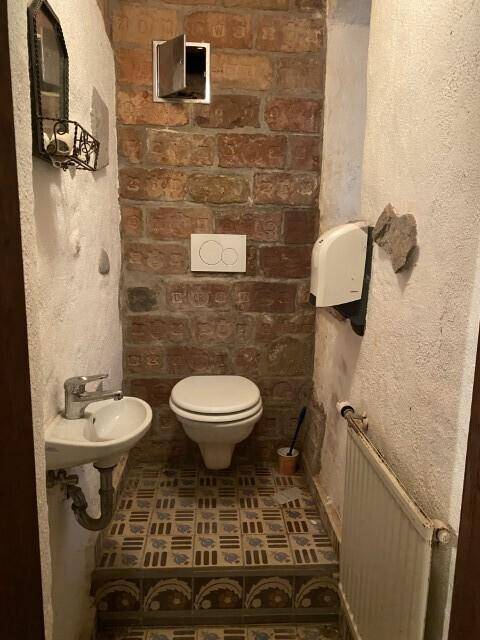 Kleine Toilette mit einem Wand-WC, einem Handwaschbecken und gemusterten Bodenfliesen, einfach und funktional.