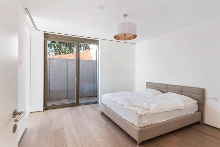 Modernes Schlafzimmer mit Holzboden, großem Bett und Zugang zu einem kleinen Außenbereich.
