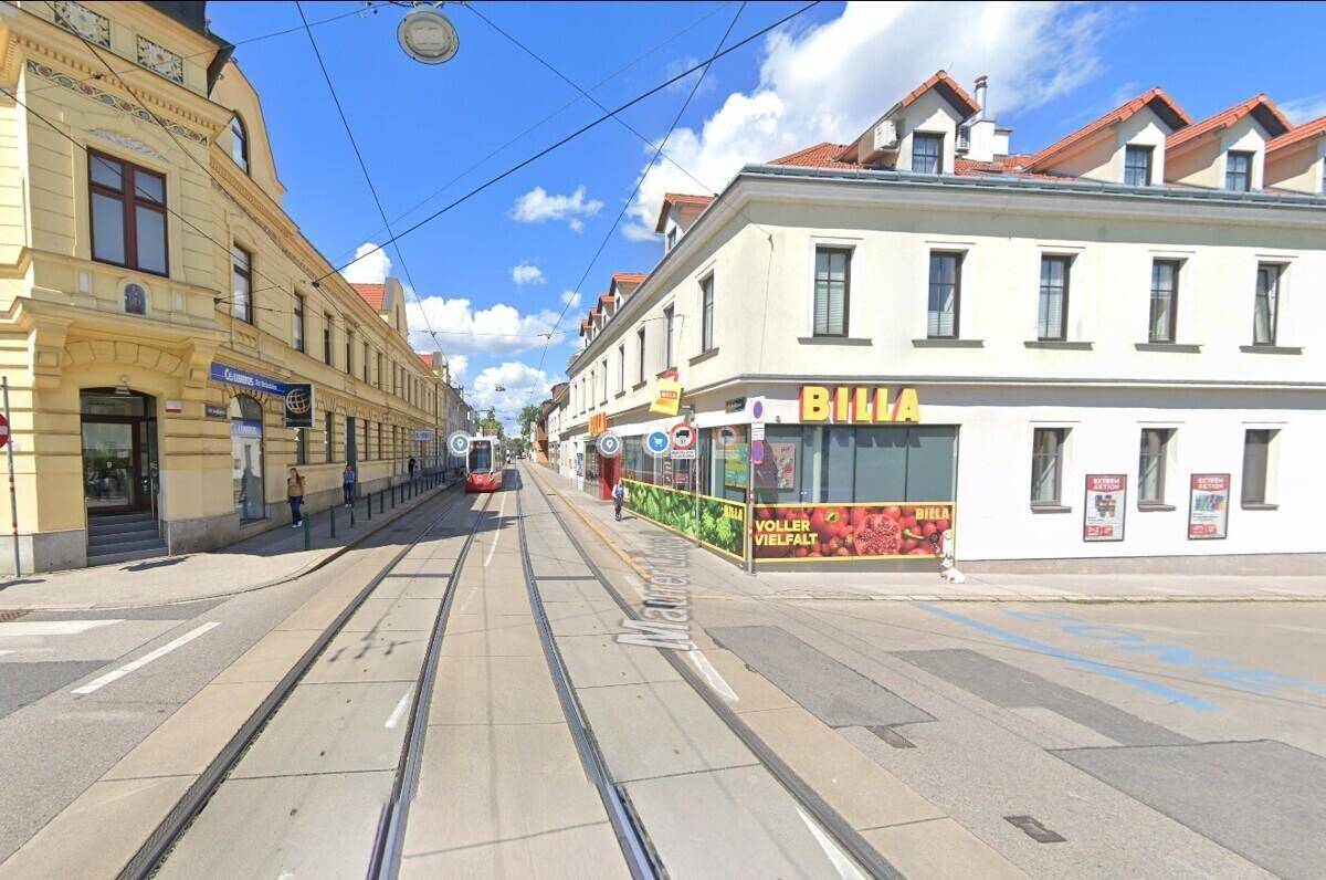 Belebte Stadtstraße mit Straßenbahnschienen, Geschäften und historischen Gebäuden unter blauem Himmel.