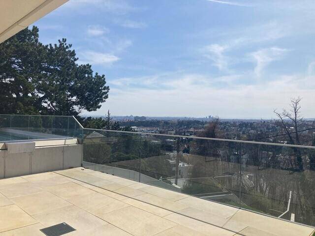 Geräumige Terrasse mit hellen Fliesen, Glasgeländer und Panoramablick über die Stadt und die Natur.
