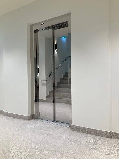 Moderner Aufzugsbereich mit Spiegeltüren und angrenzendem Treppenhaus, hell und funktional.