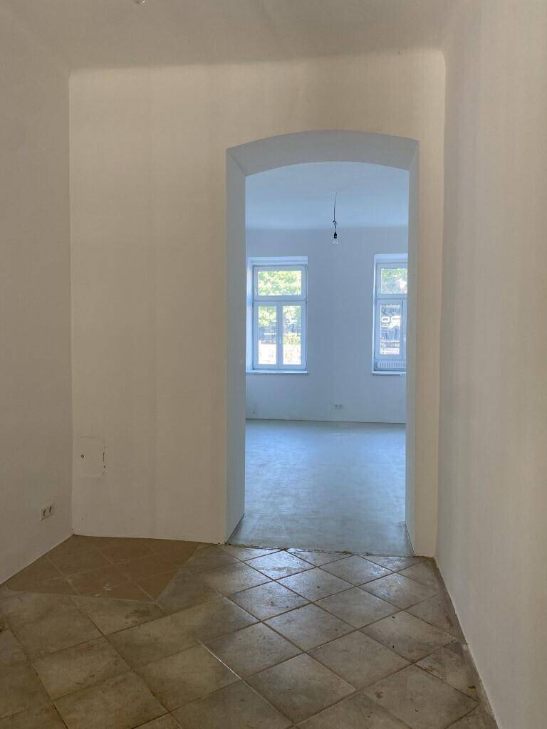 Flur mit hellen Fliesen und einem Durchgang, der den Blick in einen weiteren, leeren Raum freigibt.