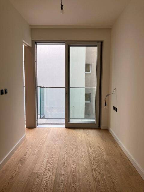 Lichtdurchflutetes Zimmer mit Holzboden und Zugang zu einem Balkon, bereit zur individuellen Gestaltung.