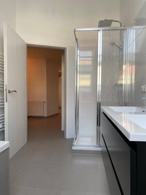 Modernes Badezimmer mit Doppelwaschbecken und Duschkabine, hell gefliest.
