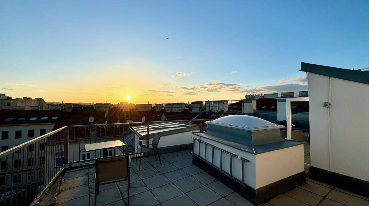 Weitläufige Dachterrasse mit Stadtblick und Sitzgelegenheiten bei Sonnenuntergang.