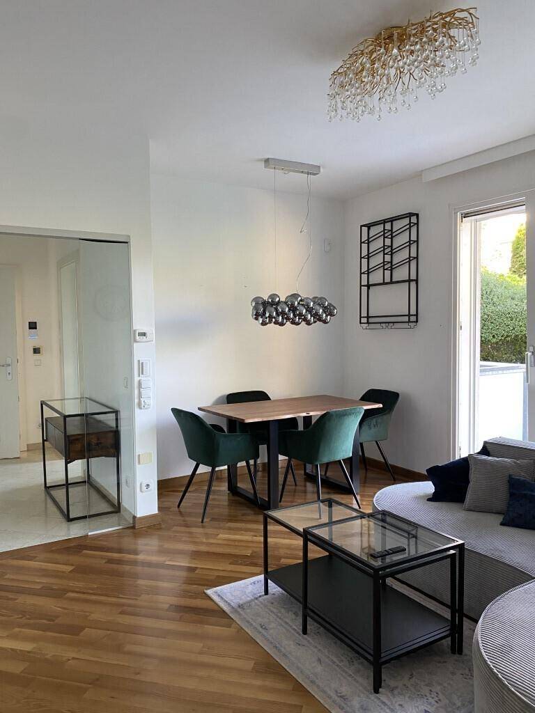 Heller Wohn- und Essbereich mit Holzboden, modernem Sofa und Zugang zum Balkon.