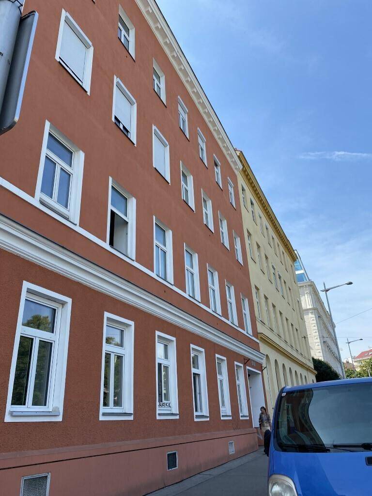 Mehrstöckiges Wohngebäude mit roter Fassade, vielen Fenstern und weißen Fensterläden an einem sonnigen Tag.