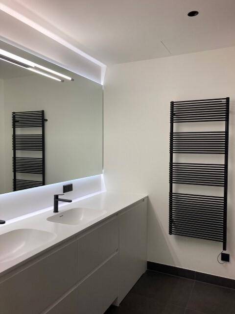Elegantes Badezimmer mit Doppelwaschbecken, beleuchtetem Spiegel und schwarzem Handtuchheizkörper.
