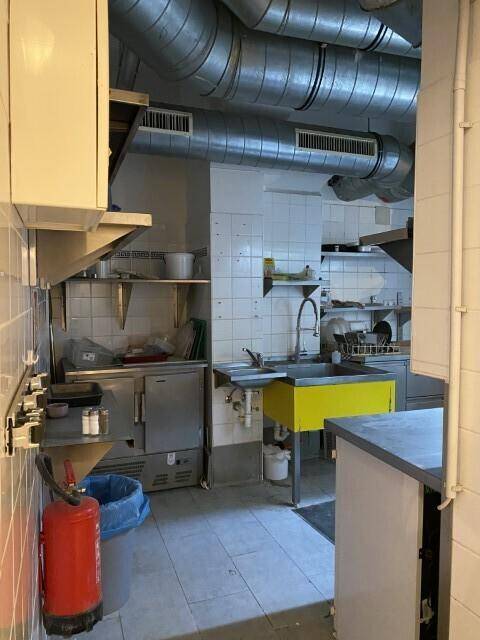 Professionelle Restaurantküche mit gefliesten Wänden, Edelstahlgeräten und einem Feuerlöscher, bereit für den täglichen Gebrauch.